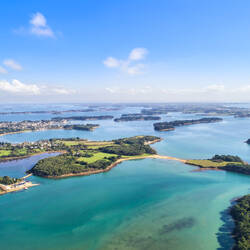 Morbilhan : Vue aérienne de nombreuses petites îles verdoyantes éparpillées dans une mer turquoise et peu profonde, sous un ciel bleu avec quelques nuages blancs.