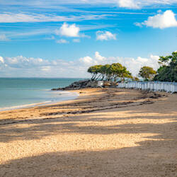 Vendée: Light sandy beach with rows of white cabins, bordered by a turquoise sea and a blue sky with scattered white clouds.