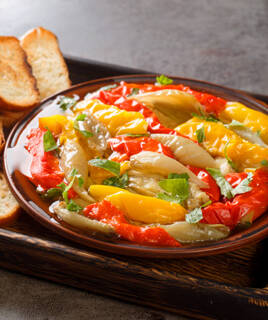 Plat d'Escalivada, une spécialité catalane, composé de poivrons rouges et jaunes rôtis, d'aubergines et d'oignons, garni de persil frais, servi avec des tranches de pain grillé sur un plateau en bois.