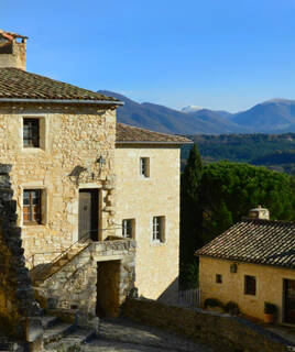 Maisons en pierre traditionnelles du village perché du Poët-Laval, avec un paysage de montagnes en arrière-plan sous un ciel clair.