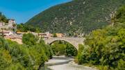Le Pont Roman de Nyons enjambant la rivière l'Aygues, avec la ville de Nyons et une colline verdoyante en arrière-plan.