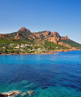 Vue aérienne du Massif de l'Esterel et d'Anthéor, près de Saint-Raphaël, montrant ses falaises de roche rouge plongeant dans les eaux bleues de la Méditerranée, avec des maisons blanches nichées sur le littoral.