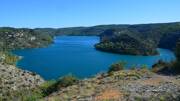 Les eaux calmes et profondes du Lac d'Esparron, aux teintes vertes et bleues, bordées par des falaises calcaires et une végétation méditerranéenne luxuriante, dans les Gorges du Verdon.