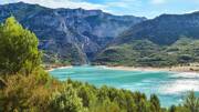 Vue imprenable sur les eaux turquoise du Lac de Sainte-Croix, dans les Gorges du Verdon, avec ses rives boisées et les falaises calcaires en arrière-plan sous un ciel dégagé.