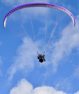 Un parapente coloré s'élance dans le ciel azur au-dessus des paysages des Gorges du Verdon, offrant une vue imprenable sur les environs et le Lac de Sainte-Croix.