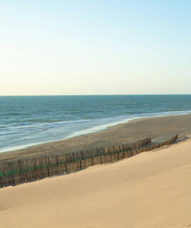 Une plage de sable s'étendant vers l'océan Atlantique, avec des clôtures en bois pour retenir le sable des dunes.
