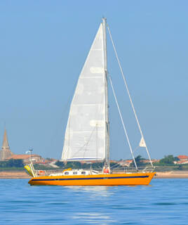 Image d'un voilier orange sur l'eau, avec le clocher de l'église de Saint-Martin-de-Ré et des maisons en arrière-plan, sur l'Île de Ré.