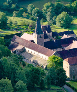 Vue aérienne de l'Abbaye de Baume-les-Messieurs et ses bâtiments entourés de verdure.