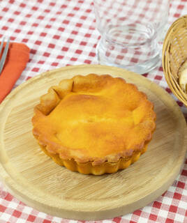 Une tourte salée dorée, ressemblant à une Tielle sétoise, posée sur une planche en bois sur une nappe à carreaux rouges et blancs, typique de la cuisine Héraultaise.