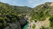 Le Pont du Diable traversant les Gorges de l'Hérault, avec la rivière sinueuse au fond d'un canyon verdoyant sous un ciel partiellement nuageux.