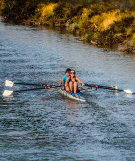 Deux personnes souriantes faisant du kayak sur la rivière de l'Hérault, au cœur des Gorges de l'Hérault, avec une végétation dense sur les rives.