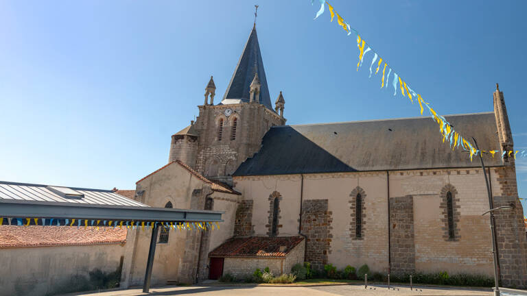 L'Église Notre-Dame de Longeville-sur-Mer, avec son clocher pointu et ses murs en pierre, sous un ciel ensoleillé, décorée de guirlandes festives.
