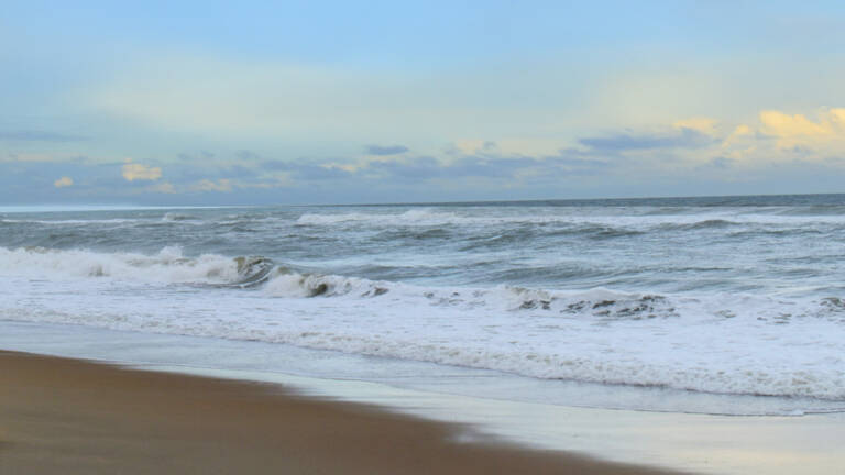 Plage des Conches à Longeville-sur-Mer : Vue sur l'océan avec des vagues déferlantes sur une plage de sable, sous un ciel partiellement nuageux.