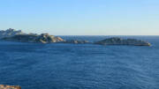 Vue panoramique sur l'archipel du Frioul près de Marseille, montrant ses îles rocheuses émergeant des eaux bleues profondes de la Méditerranée sous un ciel clair, avec une partie du Massif des Calanques visible à l'horizon.