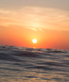 Coucher de soleil orange sur l'océan, avec le soleil visible juste au-dessus des vagues, près de Contis à Mimizan.