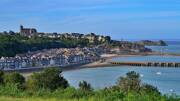 Vue panoramique de Cancale en Bretagne, avec ses maisons en bord de mer, le port, et l'église Saint-Méen au sommet de la colline, sous un ciel bleu.