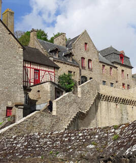 Ruelles pavées et maisons médiévales en pierre avec toits en ardoise et détails rouges, typiques du Mont Saint-Michel, sous un ciel partiellement nuageux.