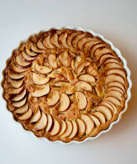 Une tarte normande dorée dans un plat de cuisson blanc, garnie de fines tranches de pommes disposées en spirale.