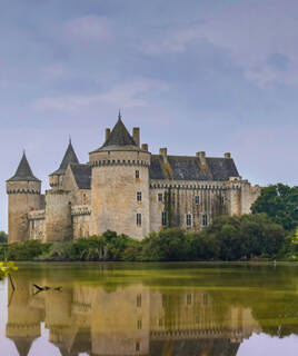 Les alignements de menhirs de Carnac, de grandes pierres dressées dans un champ verdoyant sous un ciel partiellement nuageux, avec des arbres en arrière-plan.