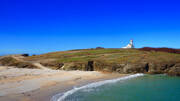 Le phare de Goulphar sur Belle-Île-en-Mer, dominant une plage de sable et la mer turquoise sous un ciel bleu intense.