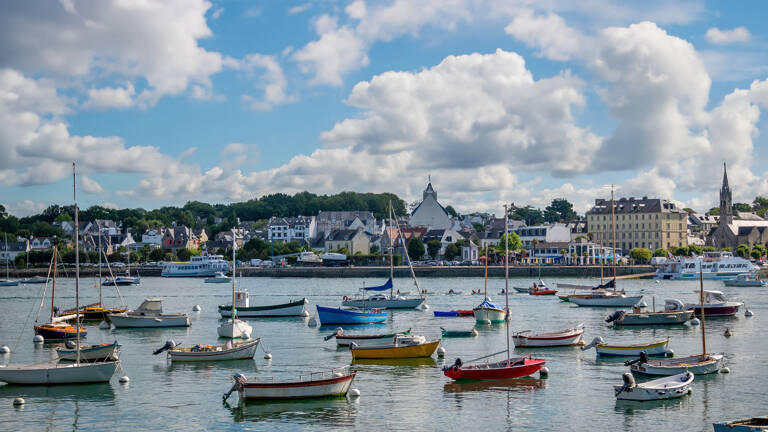 Vue du port de Bénodet avec de nombreux bateaux de plaisance et le bourg en arrière-plan sous un ciel nuageux.