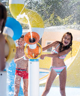 Enfants riant et jouant dans une aire de jeux aquatique avec des jets d'eau, probablement dans un camping ou un parc aquatique.