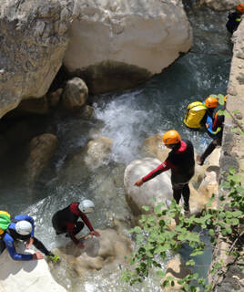 Des personnes équipées de combinaisons de canyoning et de casques évoluent dans une rivière aux eaux claires et tumultueuses, entourée de parois rocheuses, lors d'une activité de canyoning dans les environs de Porto-Vecchio en Corse.