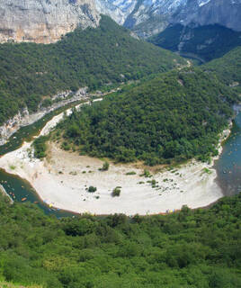 Vallée verdoyante avec une rivière sinueuse et ses méandres, parsemée de kayaks, dans le Cirque de Gens en Ardèche, près de Vallon-Pont-d'Arc.