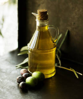Bouteille d'huile d'olive avec des olives vertes et noires et une branche d'olivier, symbolisant la production locale près de Vallon-Pont-d'Arc.