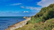 Chemin côtier herbeux surplombant la mer, avec un ciel bleu et quelques nuages, sur la Presqu'île de Rhuys, près de Vannes.