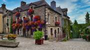 Rue pavée de Rochefort-en-Terre, près de Vannes, avec des maisons en pierre fleuries de géraniums rouges et violets.