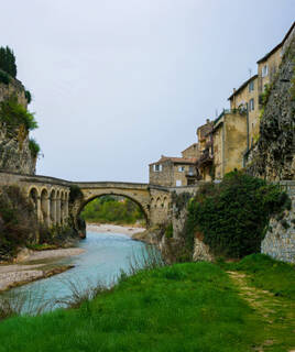 Le Pont Romain de Vaison-la-Romaine, une structure ancienne enjambant une rivière, avec des bâtiments en pierre de la vieille ville en arrière-plan, dans le Vaucluse.
