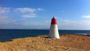 Phare rouge et blanc du Cap Rousset sur une côte rocheuse, avec la mer Méditerranée et le ciel bleu en arrière-plan, à Carry-le-Rouet.