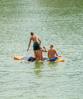 Des enfants jouant et se baignant autour d'une planche de paddle gonflable sur les eaux calmes à L'Aiguillon-sur-Mer, sous un ciel ensoleillé.