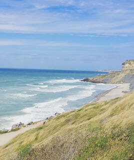La côte d'Opale près du Touquet, avec ses falaises abruptes et sa plage de galets bordée par les vagues de la Manche, sous un ciel parsemé de nuages.