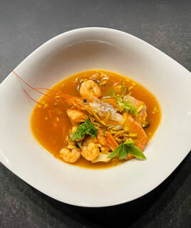 Un plat de spécialité culinaire du Touquet-Paris-Plage, composé d'une soupe riche en fruits de mer avec des crevettes, des moules et d'autres poissons dans un bouillon orangé, garni d'herbes fraîches.