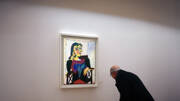 Un visiteur, vu de dos, contemple un tableau de Picasso représentant une femme assise, exposé au Musée Picasso de Barcelone, sur un mur blanc et dans une lumière de galerie.