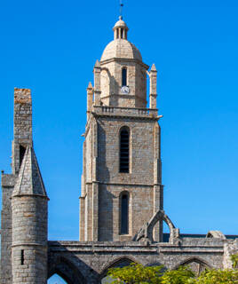 Détail de la tour en pierre de l'Église Saint-Guénolé à Batz-sur-Mer, sur fond de ciel bleu éclatant, avec des éléments d'arches et de ruines sur les côtés.