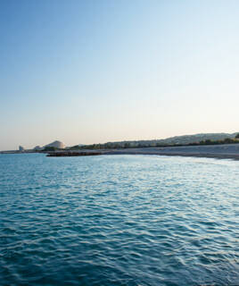 La plage de galets de Cagnes-sur-Mer, bordée par les eaux bleues de la Méditerranée et des collines lointaines, sous un ciel clair au lever ou au coucher du soleil.