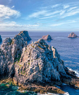 La Pointe de Pen-Hir à Camaret-sur-Mer, avec ses impressionnants rochers escarpés émergeant de l'océan Atlantique, sous un ciel bleu parsemé de nuages blancs.