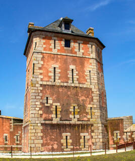La Tour Vauban à Camaret-sur-Mer, une tour fortifiée en pierre de couleur ocre avec un toit d'ardoise, se dressant sous un ciel bleu clair.