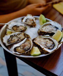 Un plateau d'huîtres fraîches sur un lit de glace avec des quartiers de citron vert, typique d'une dégustation au Cap Ferret, posé sur une table en bois.