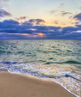La plage de Capbreton au coucher du soleil, avec des vagues douces s'écrasant sur le sable, et un ciel teinté de couleurs violettes et orangées à l'horizon.