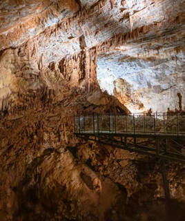 L'intérieur majestueux du Gouffre de Cabrespine, près de Carcassonne, révélant d'immenses stalactites et stalagmites illuminées, avec une passerelle métallique permettant l'exploration souterraine.