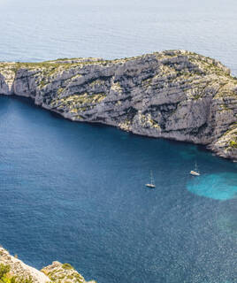 Une vue aérienne des Calanques de Marseille, près de Carry-le-Rouet, révélant des falaises calcaires escarpées plongeant dans les eaux turquoise de la Méditerranée, avec deux voiliers naviguant paisiblement.