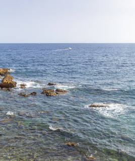 La mer Méditerranée avec des rochers affleurant près de la côte à Carry-le-Rouet, sous un ciel clair, avec un bateau lointain sur l'eau.