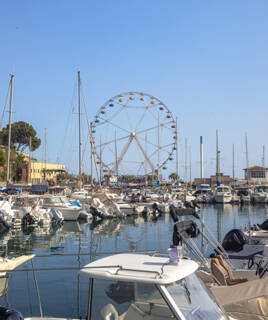 Le port de plaisance de Carry-le-Rouet, rempli de nombreux bateaux amarrés, avec une grande roue colorée visible en arrière-plan sous un ciel bleu dégagé.