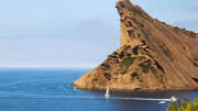Le Bec de l'Aigle, une imposante falaise rocheuse surplombant la Baie de La Ciotat, près de Cassis, avec des bateaux naviguant sur les eaux bleues de la Méditerranée sous un ciel clair.