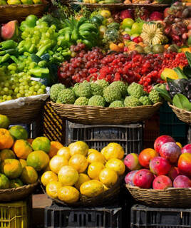 Een kleurrijke marktkraam in Cassis, waar een overvloed aan vers seizoensfruit wordt aangeboden, zoals mango's, sinaasappels en verschillende soorten druiven, gepresenteerd in manden en kratten.