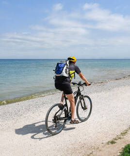 Une personne à vélo sur un chemin de terre longeant la plage du Croisic en Loire-Atlantique, avec l'océan Atlantique en arrière-plan sous un ciel bleu parsemé de nuages blancs.